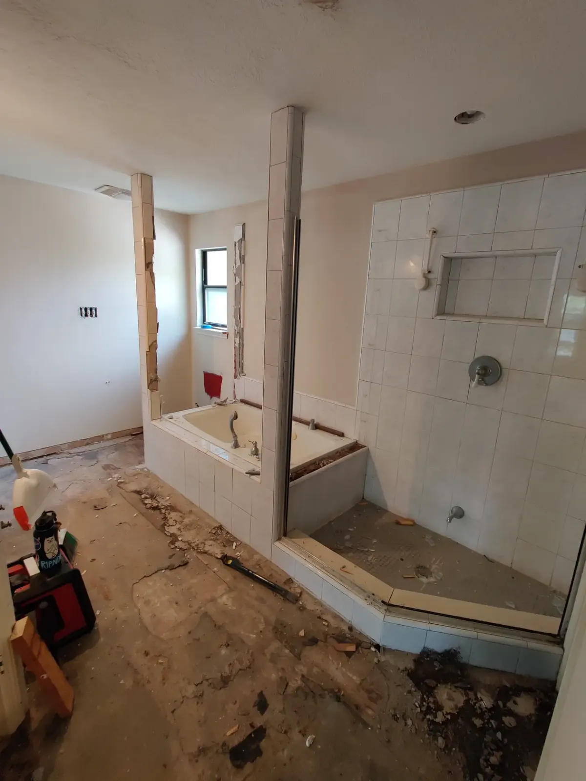 Bathroom before renovation, with the old tub surround, dated tile, and flooring removed